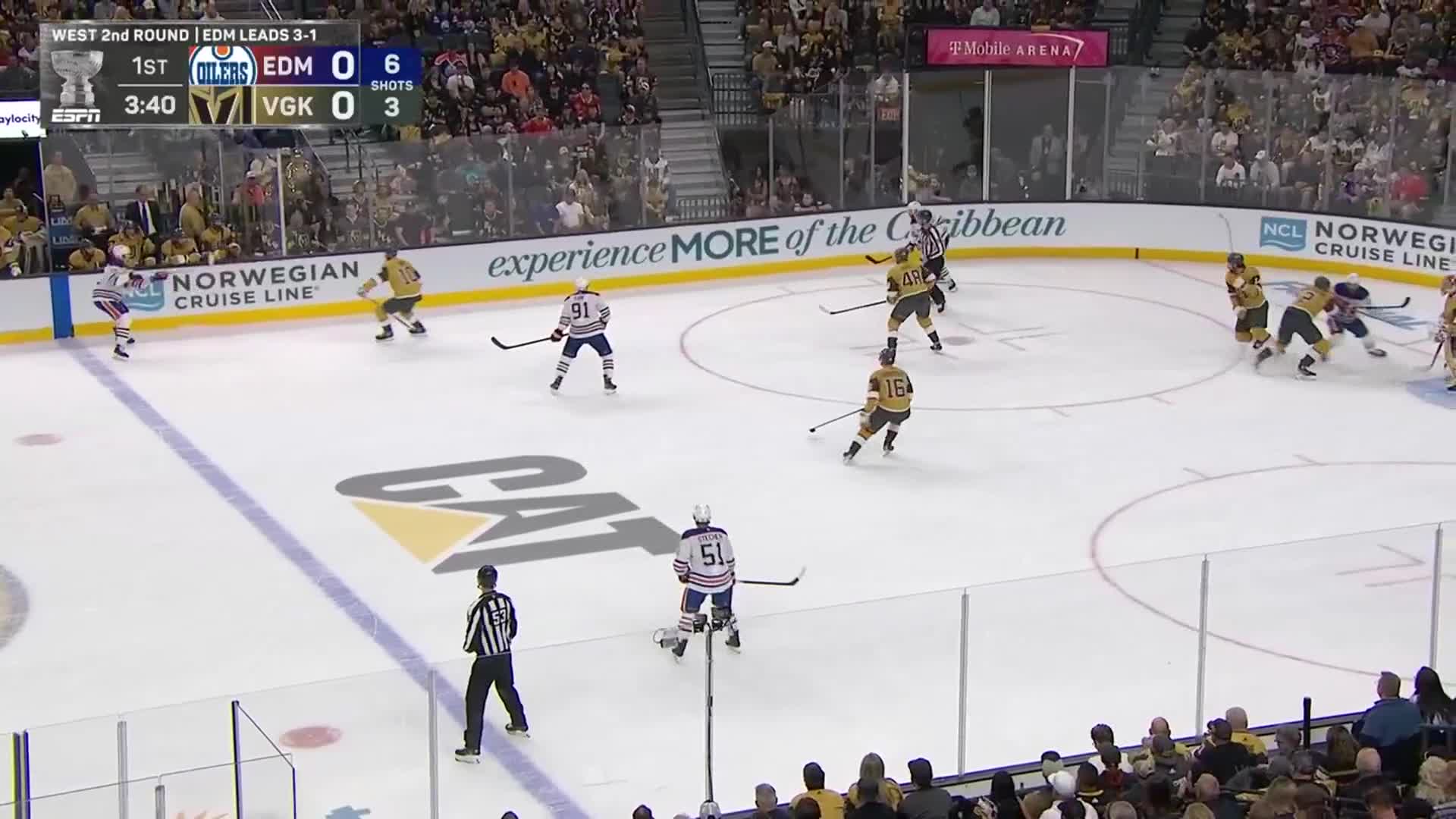 The Edmonton Oilers are in their blue and white, skating towards the goal. A referee in black and white stripes watches the play closely as the Vegas Golden Knights in gold try to gain possession.
