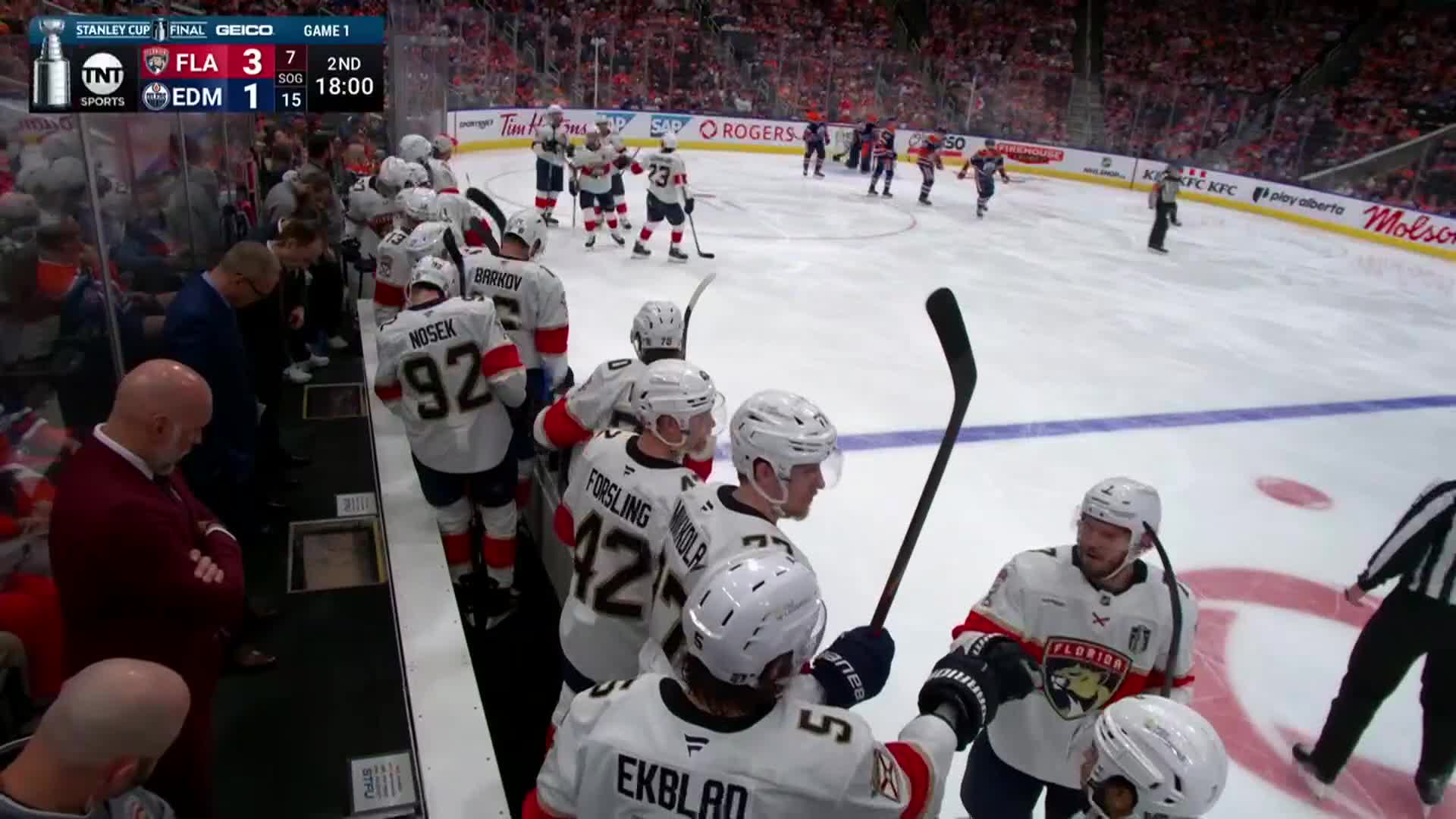 The Florida Panthers huddle on the bench, celebrating as the Edmonton Oilers skate toward their own bench. The score is displayed on the NHL Network broadcast, showing the Panthers with a comfortable lead.
