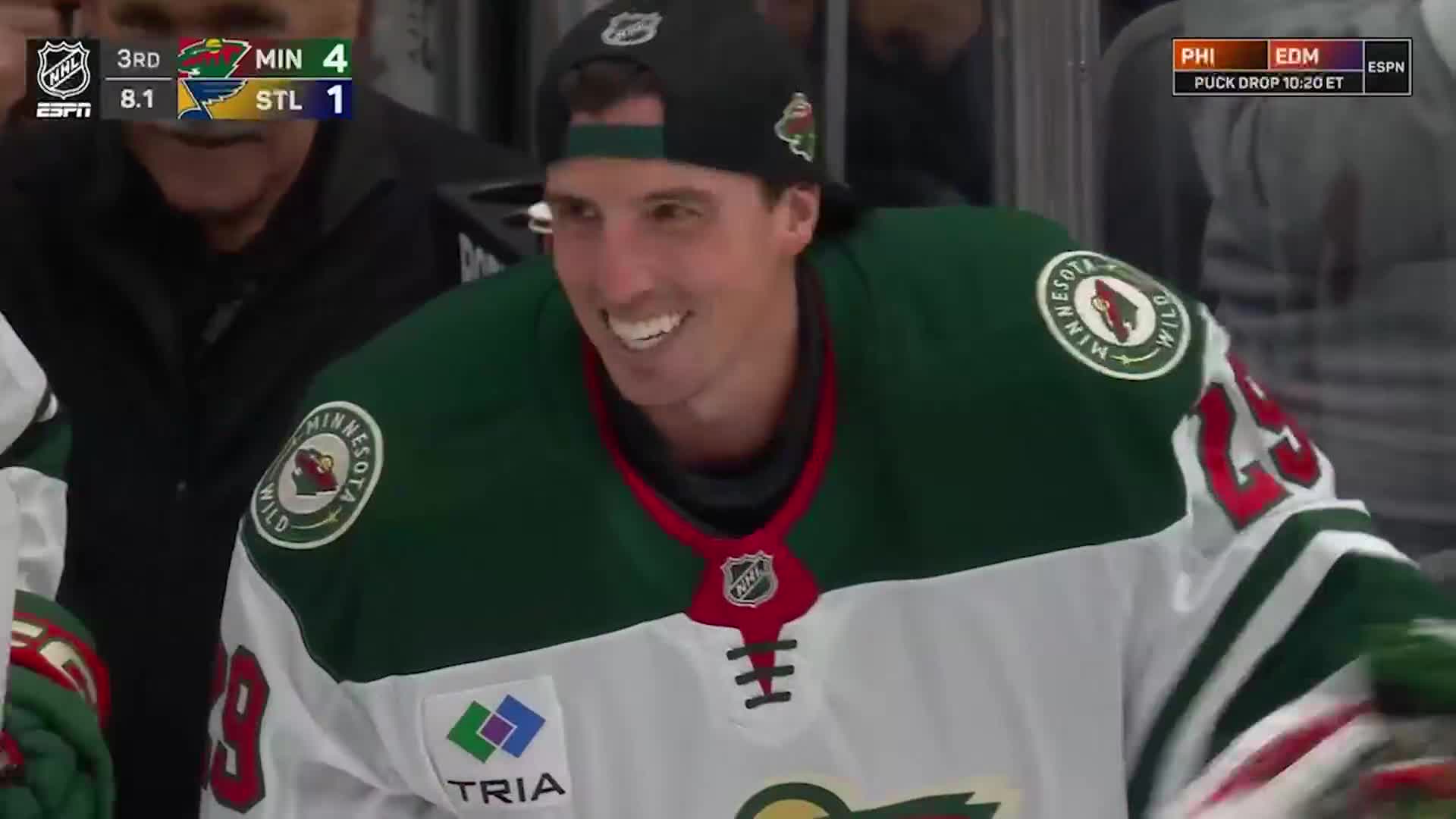 The Minnesota Wild player grins broadly, wearing a backwards cap and his team's jersey. The scoreboard shows the Wild leading in the third period, with the NHL Network logo visible in the corner.
