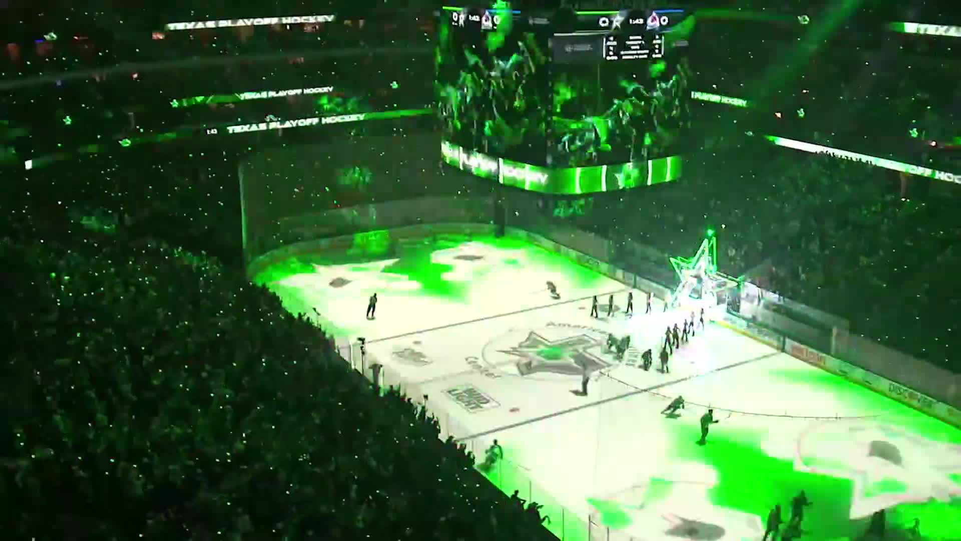 The ice is lit up in green, and the crowd is a sea of tiny lights. Players are gathering on the ice, preparing for a hockey game.
