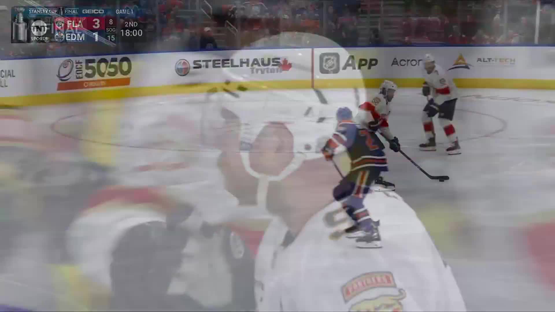 The Oilers player, in blue and orange, skates with the puck, pursued by two players in red. The score shows Florida leading Edmonton in the second period of the NHL game.
