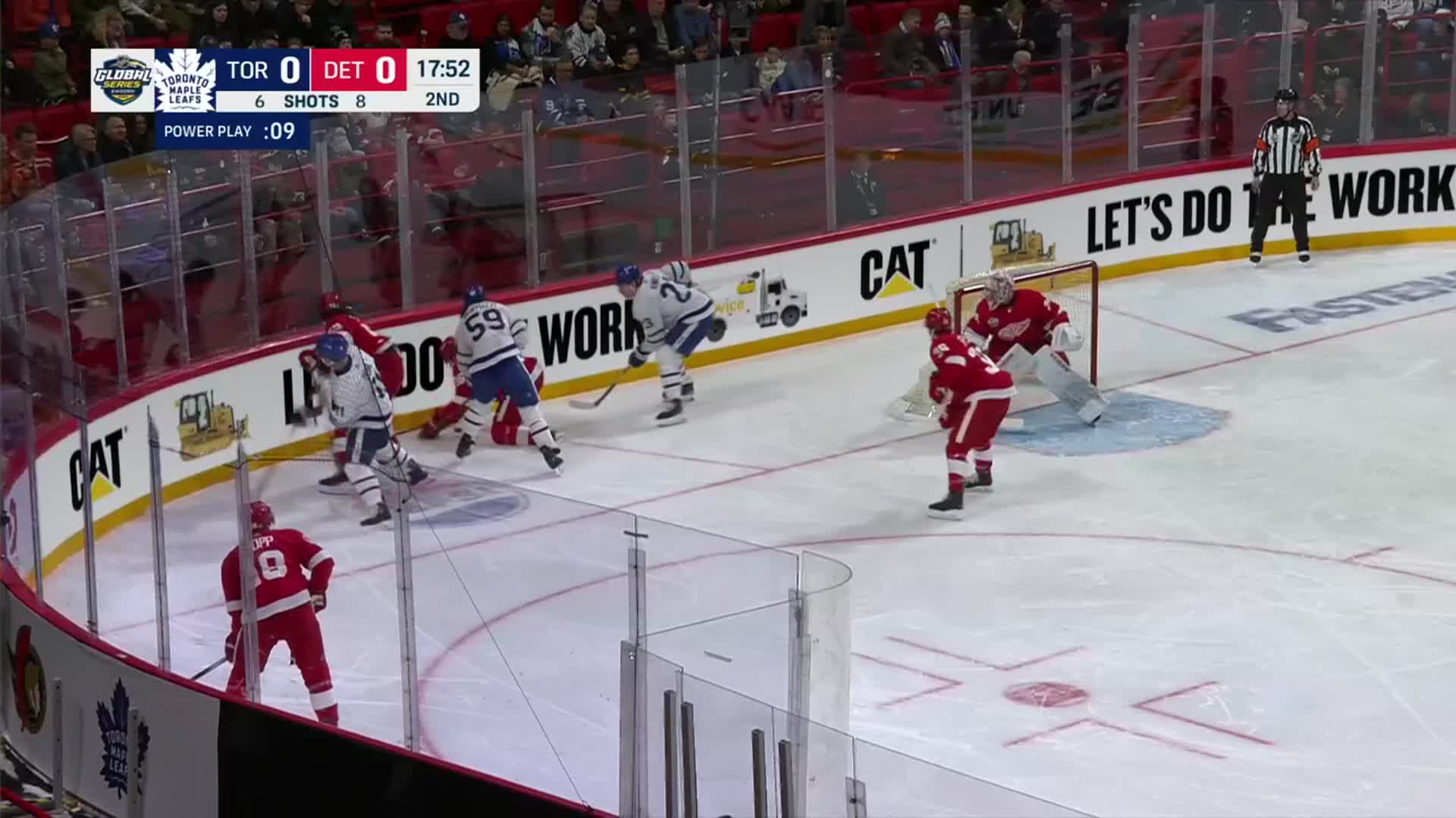 The Toronto Maple Leafs are on a power play, trying to score against the Detroit Red Wings. A scrum of players battles near the net as the goalie watches intently.
