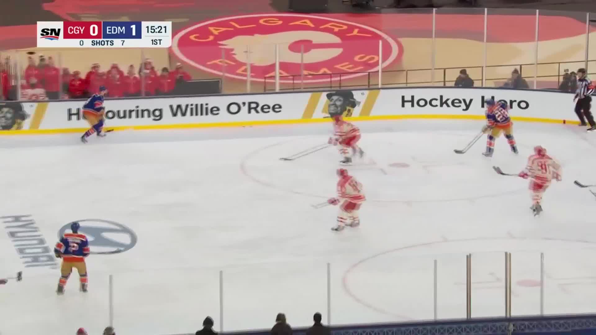 The Oilers player in blue and orange skates up the ice, stick on the puck. Calgary's players in red and white try to close him down, but the Oilers already have a goal in the first period.
