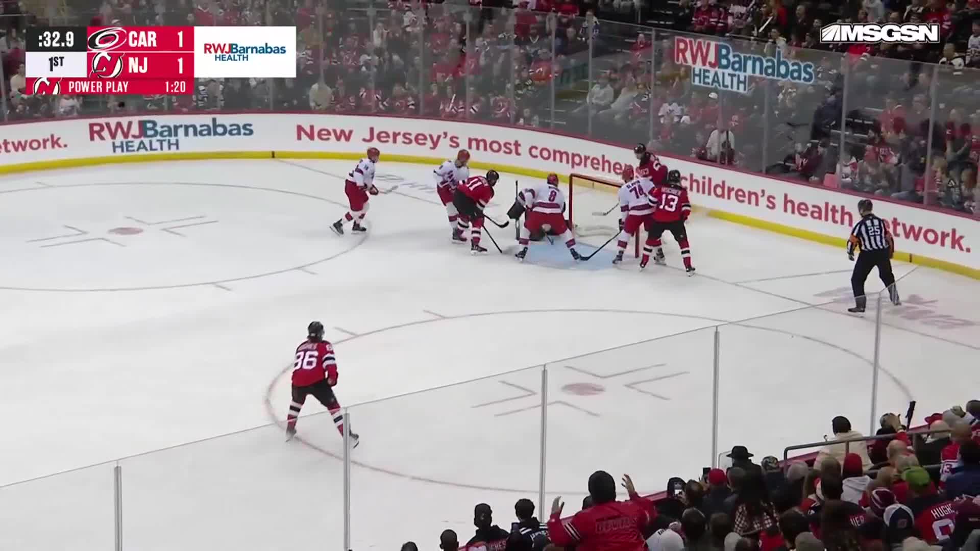The puck is near the net, with players in red and white jerseys battling for position. A referee stands nearby, watching the play unfold during the NHL game.
