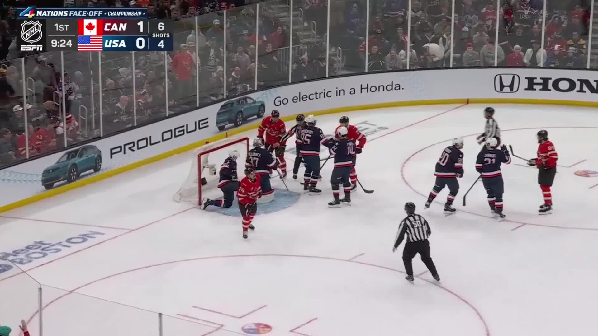 A scrum has formed around the net, with players in red and blue jerseys jostling for position. A referee in black and white stripes skates in to break up the play.