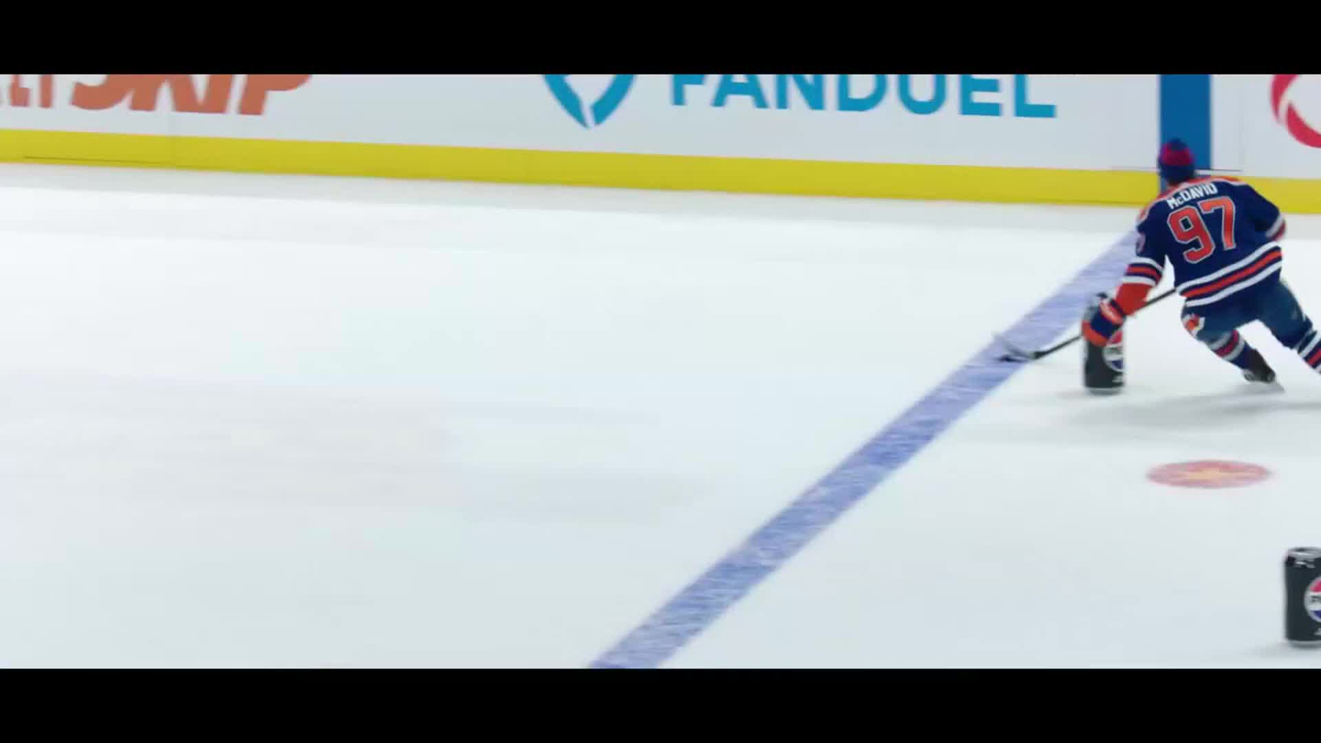 A hockey player in an orange and blue uniform skates with the puck. The NHL Network logo and FanDuel are visible on the boards behind him.