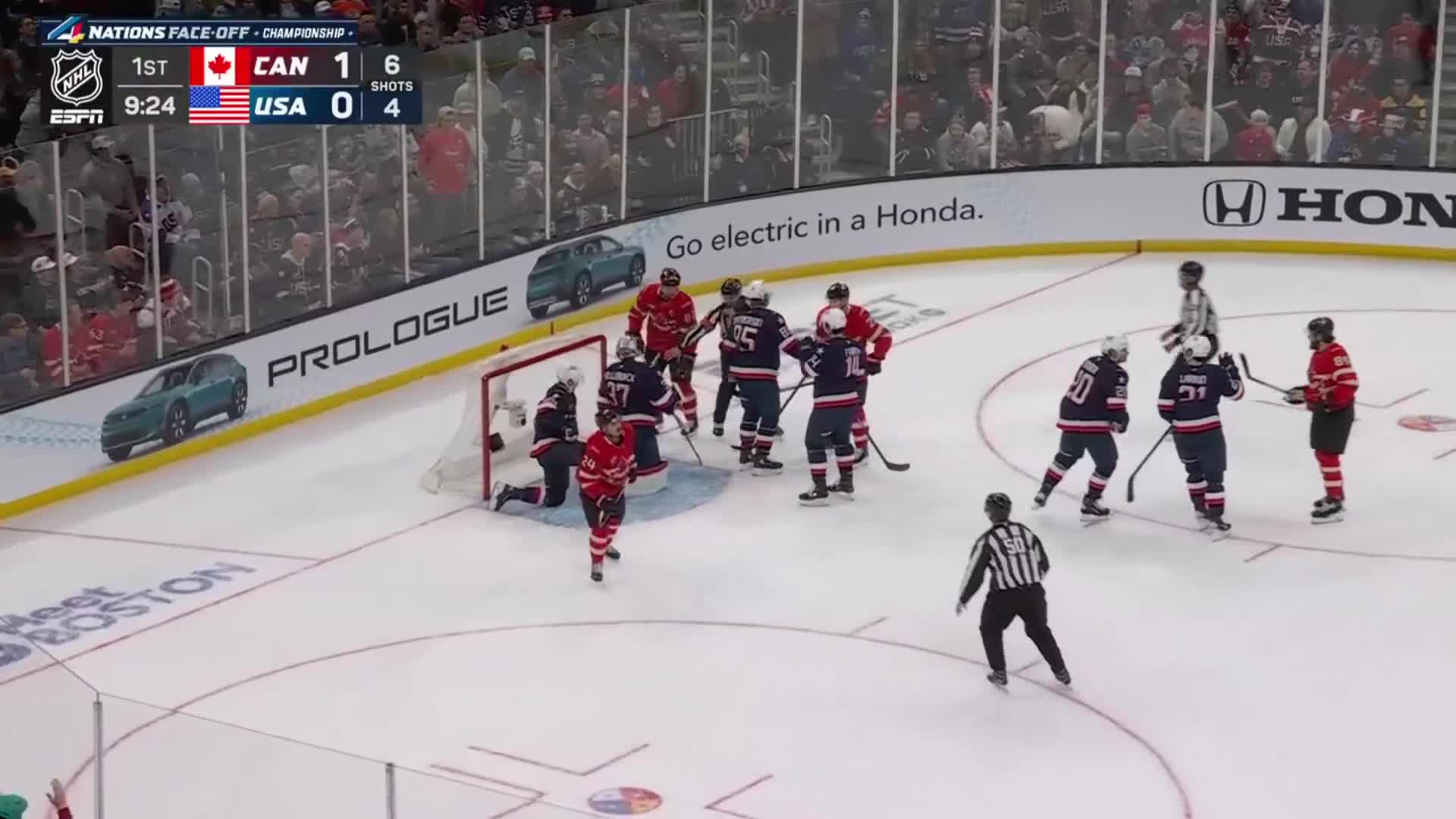 A scrum of players from Canada and the USA are tangled around the net, sticks clashing. The score shows Canada leading 1-0 in the first period.