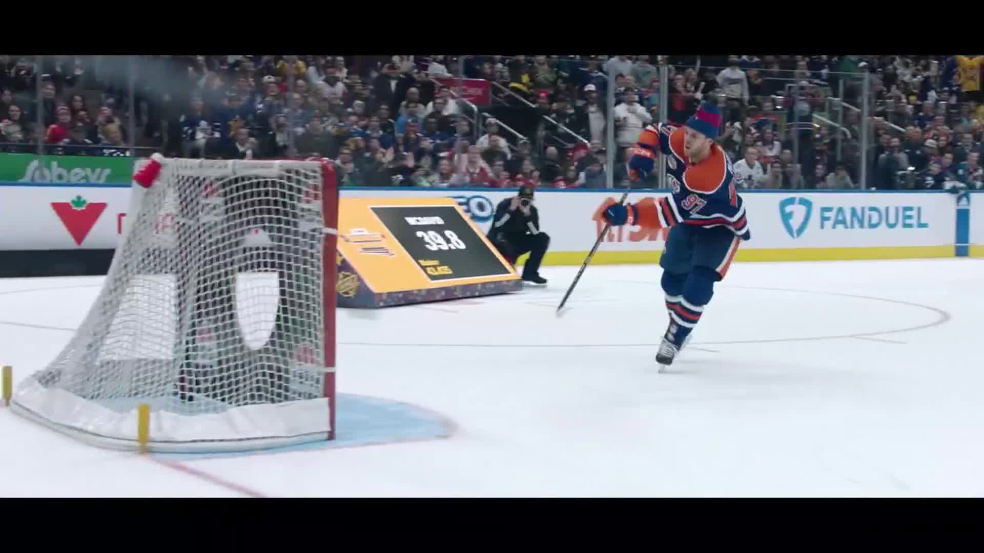 A hockey player in an orange and blue uniform skates toward the net, stick raised. A digital display behind him shows "39.8."