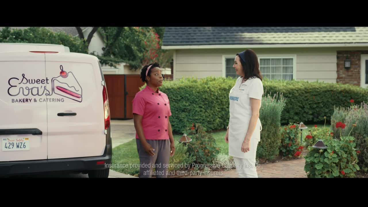 A woman in a pink chef's uniform stands next to a van advertising "Sweet Eva's Bakery & Catering," facing another woman wearing a white apron. They're on a residential street in front of a house, seemingly mid-conversation.

