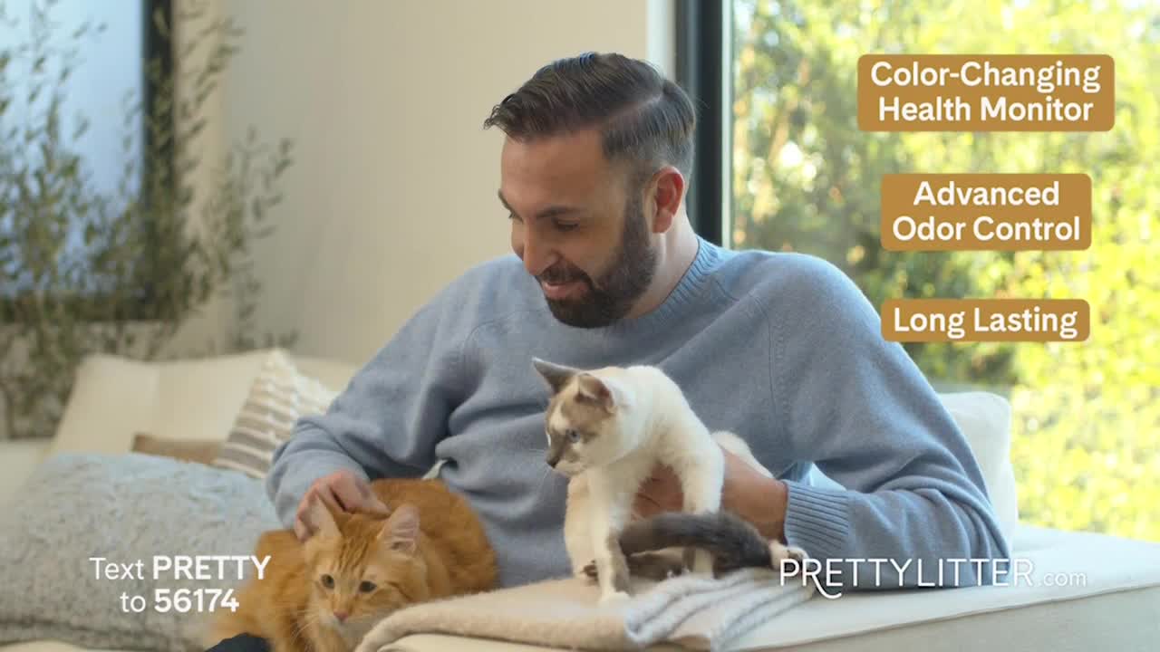 A man in a blue sweater cradles two cats in his lap, petting one while the other looks around. The scene is set in a well-lit living room, with text boxes promoting a product for cat owners.
