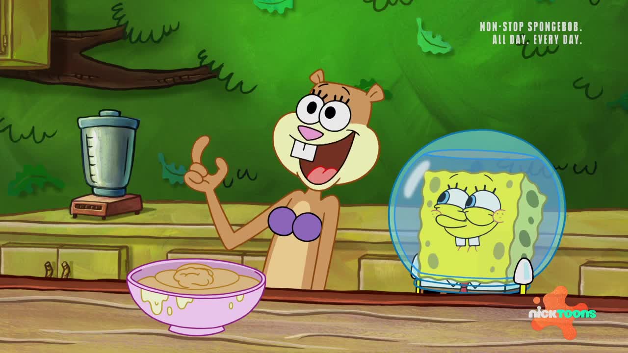 Sandy, wearing a purple bikini top, gestures excitedly towards a bowl of food. SpongeBob, encased in a bubble, grins from behind the counter.
