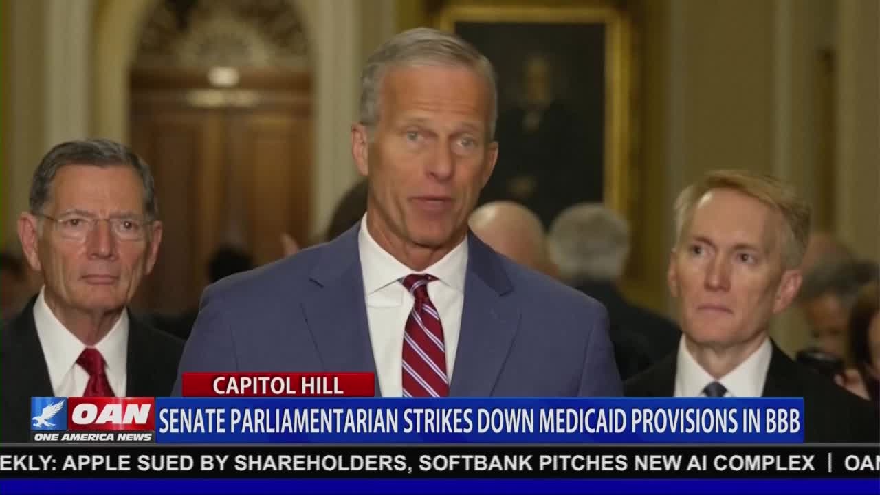 A man in a blue suit and red-striped tie speaks, framed by two other men in dark suits and red ties. The One America News Network logo and a headline about Medicaid provisions flash on the screen.
