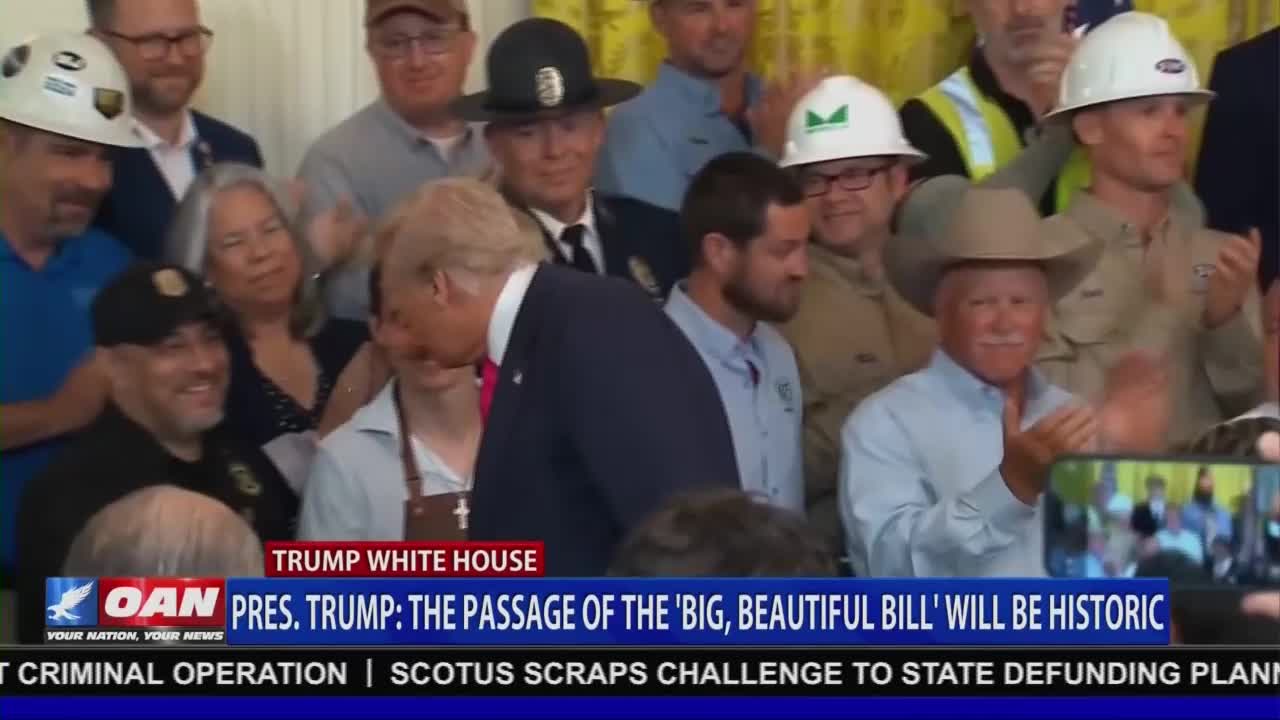 Donald Trump, in a suit and red tie, is leaning in to speak to a woman wearing an apron. Behind them, a crowd of men in hard hats and a cowboy hat clap. The news ticker at the bottom of the screen, from One America News Network, announces the passage of a bill.
