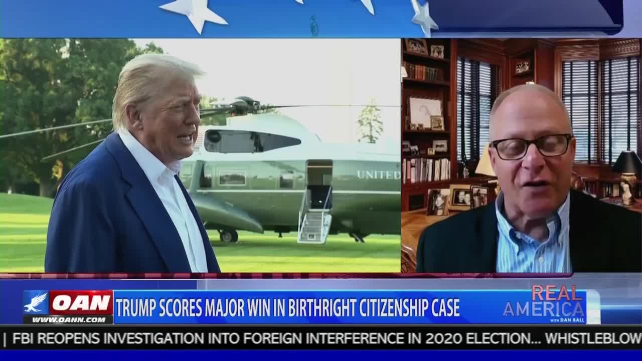 A split screen shows a man in a suit and tie speaking from a home office while a man in a blue blazer stands near a helicopter, both on the screen of a broadcast from United States-based One America News Network. The chyron reads "Trump scores major win in birthright citizenship case."
