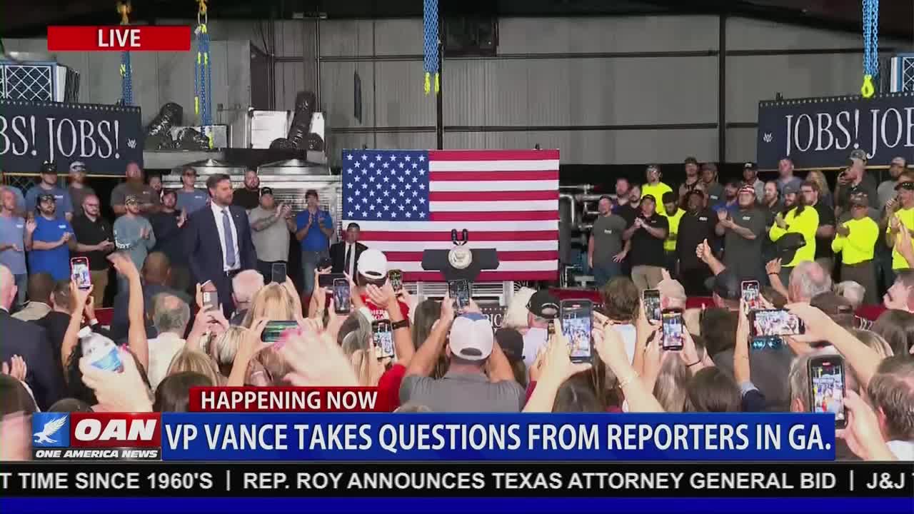 A man in a suit walks toward a podium in front of a large American flag, as a crowd of people hold up their phones. The scene is being broadcast live on One America News Network, with the words "VP Vance takes questions from reporters in GA" displayed on the screen.
