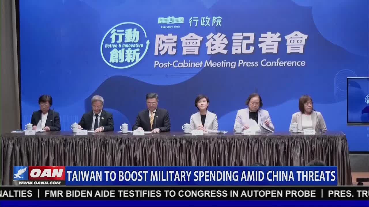 Six people sit behind a long table, facing the camera. The lower third of the screen displays a banner from OAN, reporting on Taiwan's military spending.
