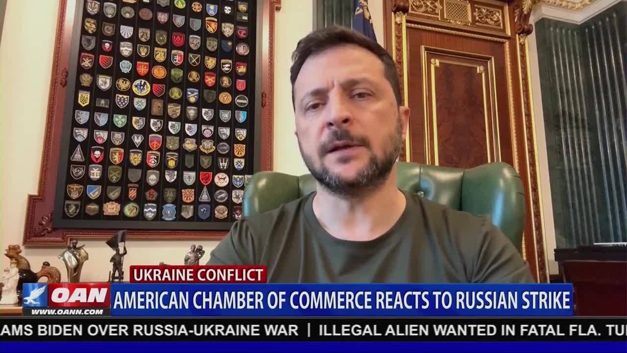 On One America News Network, a man in a green t-shirt speaks, framed by a wall of patches and ornate wood paneling. A lower third graphic identifies the segment as relating to the Ukraine conflict and the American Chamber of Commerce.
