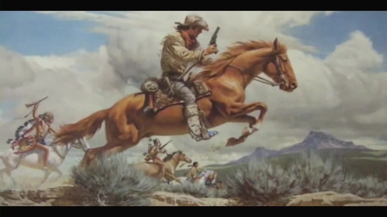 A man in a hat on a brown horse is leaping forward, his gun raised. Behind him, other riders on horseback pursue, with a mountain range in the distance.
