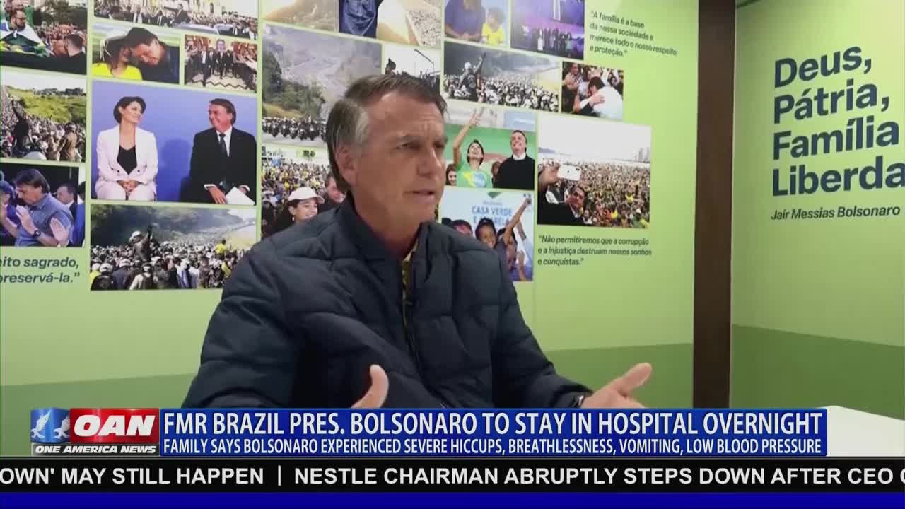 A man in a dark jacket gestures as he speaks, framed by a backdrop of photos and text. The lower third of the screen, branded by One America News, reports on the former Brazilian president's health.

