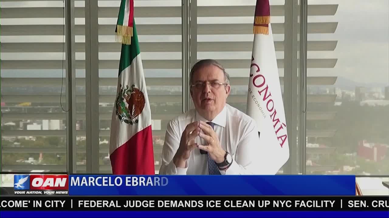 Marcelo Ebrard, speaking on One America News Network, gestures with his hands as he sits in front of two flags. The Mexican flag and a flag of the economy are visible behind him.
