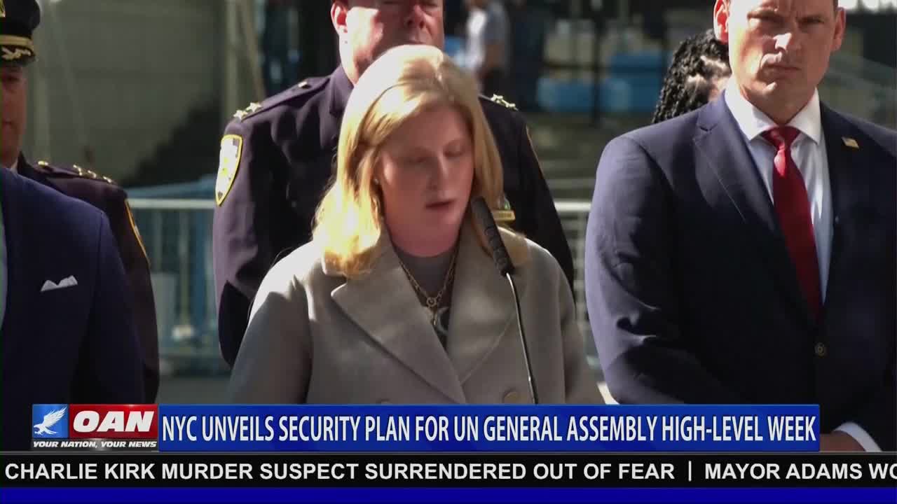 A woman in a light-colored coat speaks into a microphone, flanked by men in suits and police uniforms. The One America News Network logo and a headline about a security plan for the UN General Assembly are displayed on the screen.
