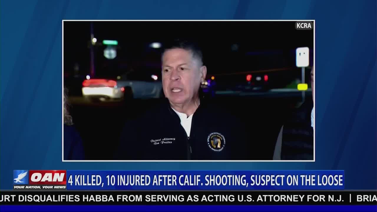 A man in a dark jacket with a badge speaks animatedly, likely for a news report. Behind him, the blurred lights of emergency vehicles and a street scene are visible on the screen, as reported by KCRA and aired on One America News Network.
