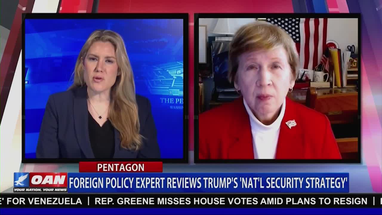 A woman in a navy blazer on the left side of the screen is speaking on One America News Network. Across from her, another woman in a red jacket is framed by an American flag and other objects, presumably in a home office.
