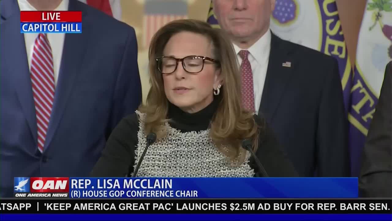 Congresswoman Lisa McClain stands at a podium, speaking to a crowd. Behind her, men in suits and flags suggest a formal event on Capitol Hill.