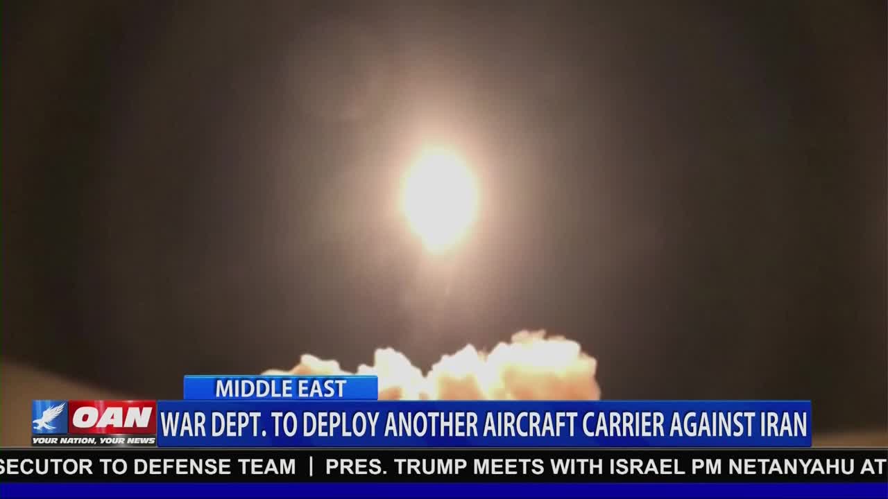 A bright light erupts from a cloud of smoke and debris. The One America News Network banner below reports the War Department is deploying another aircraft carrier against Iran.