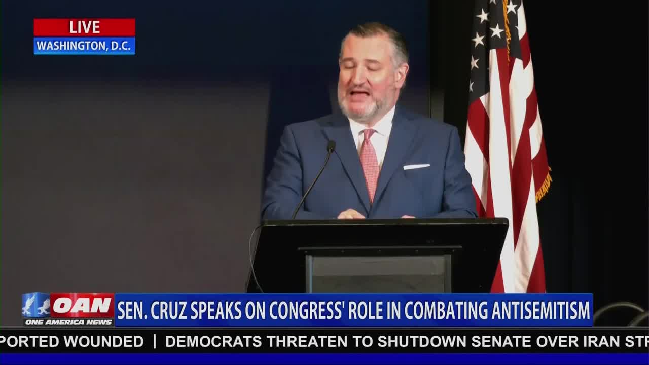 Senator Ted Cruz stands at a podium, speaking to a crowd. An American flag hangs behind him, a clear indication of the United States setting.