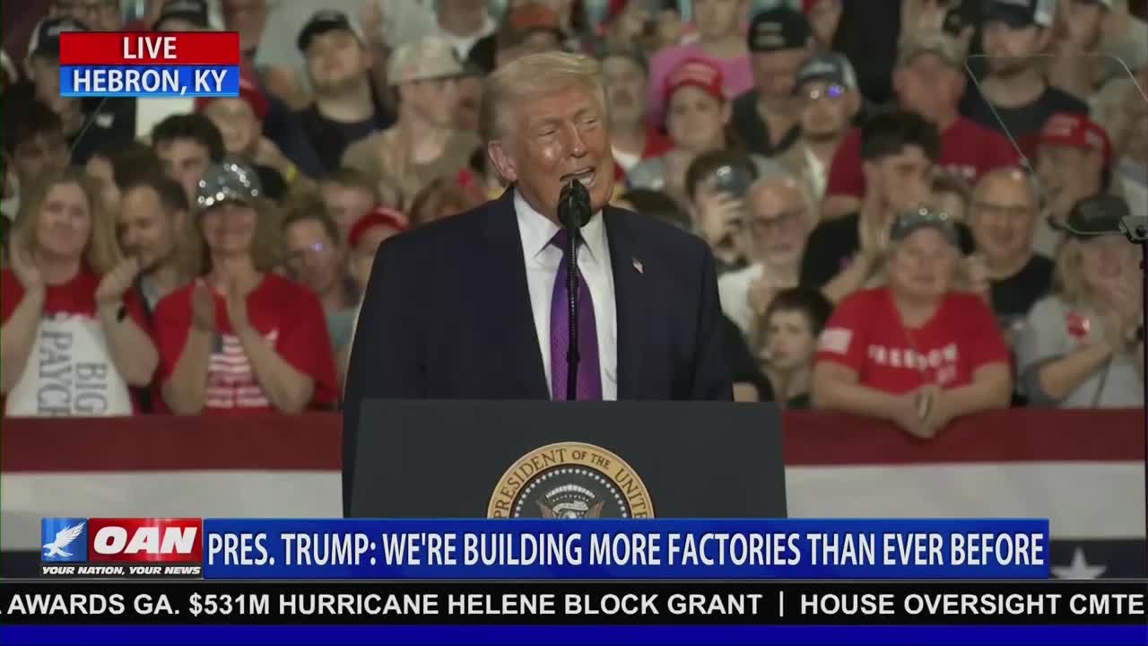 President Trump stands at a podium, speaking to a large crowd in Hebron, Kentucky. The OAN chyron reads "PRES. TRUMP: WE'RE BUILDING MORE FACTORIES THAN EVER BEFORE."