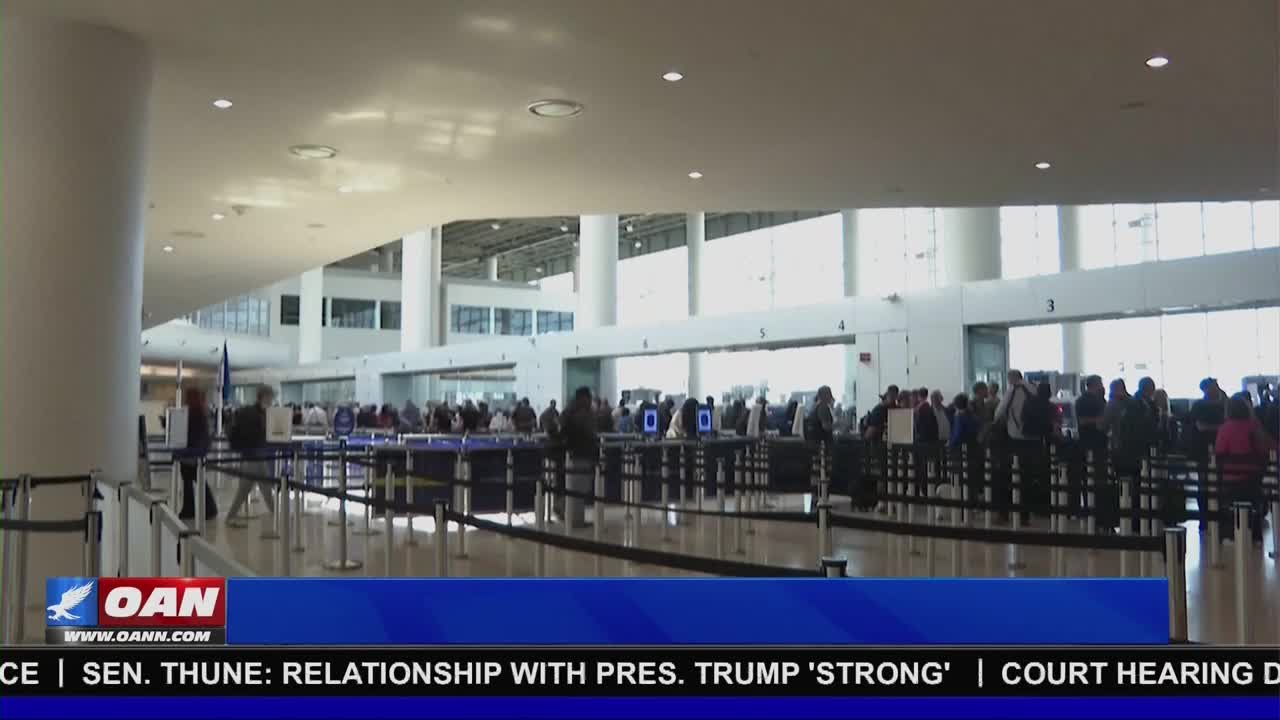 People are lining up at airport security checkpoints. A blue banner at the bottom displays "OAN" and text about a relationship with President Trump.