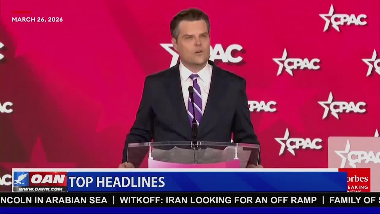 A man in a dark suit and striped tie speaks from behind a podium. The backdrop is a vibrant pink with repeating CPAC logos. A banner at the bottom displays "OAN TOP HEADLINES" and news tickers.