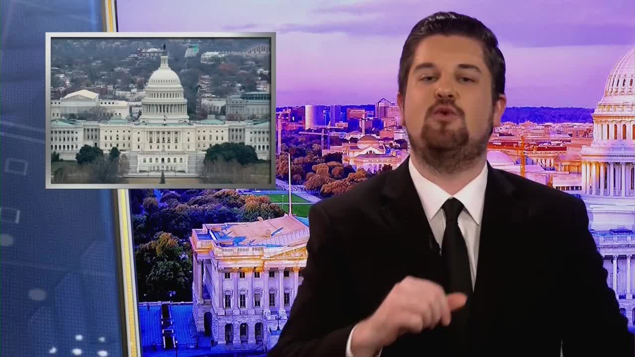 A man in a suit speaks animatedly, with the United States Capitol building displayed on a screen behind him. The backdrop also shows a city skyline at dusk.