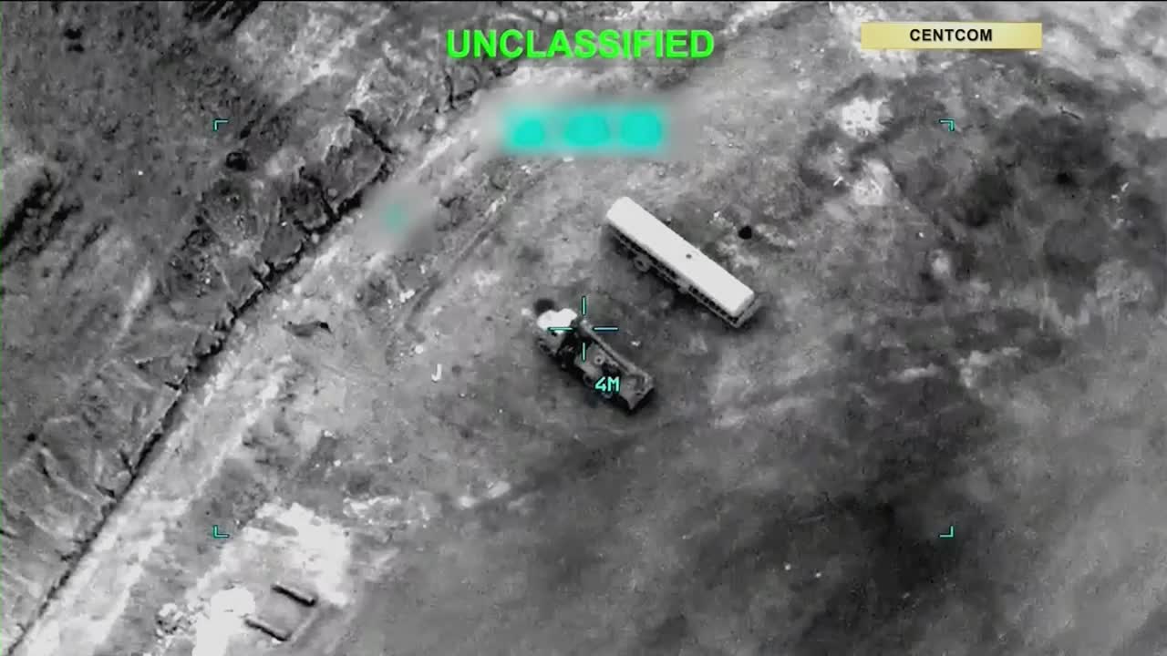 A military truck, marked with "4M," sits damaged next to a white bus.  The drone footage, marked "UNCLASSIFIED" and from CENTCOM, shows the vehicles in a desolate, rocky area.