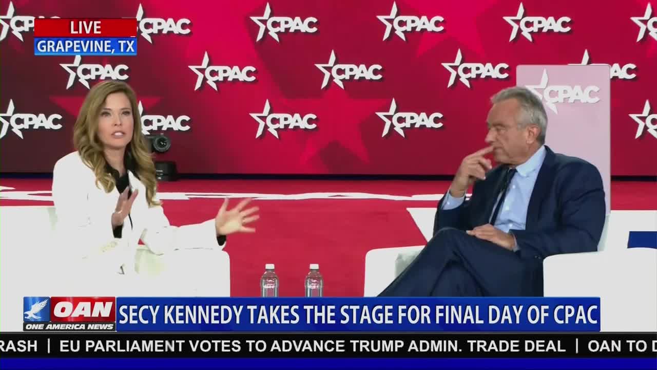 A woman in a white blazer gestures with her hands as she speaks, while a man in a dark suit leans back, his chin resting on his fingers. The One America News Network chyron indicates this is live from Grapevine, Texas, at the Conservative Political Action Conference.