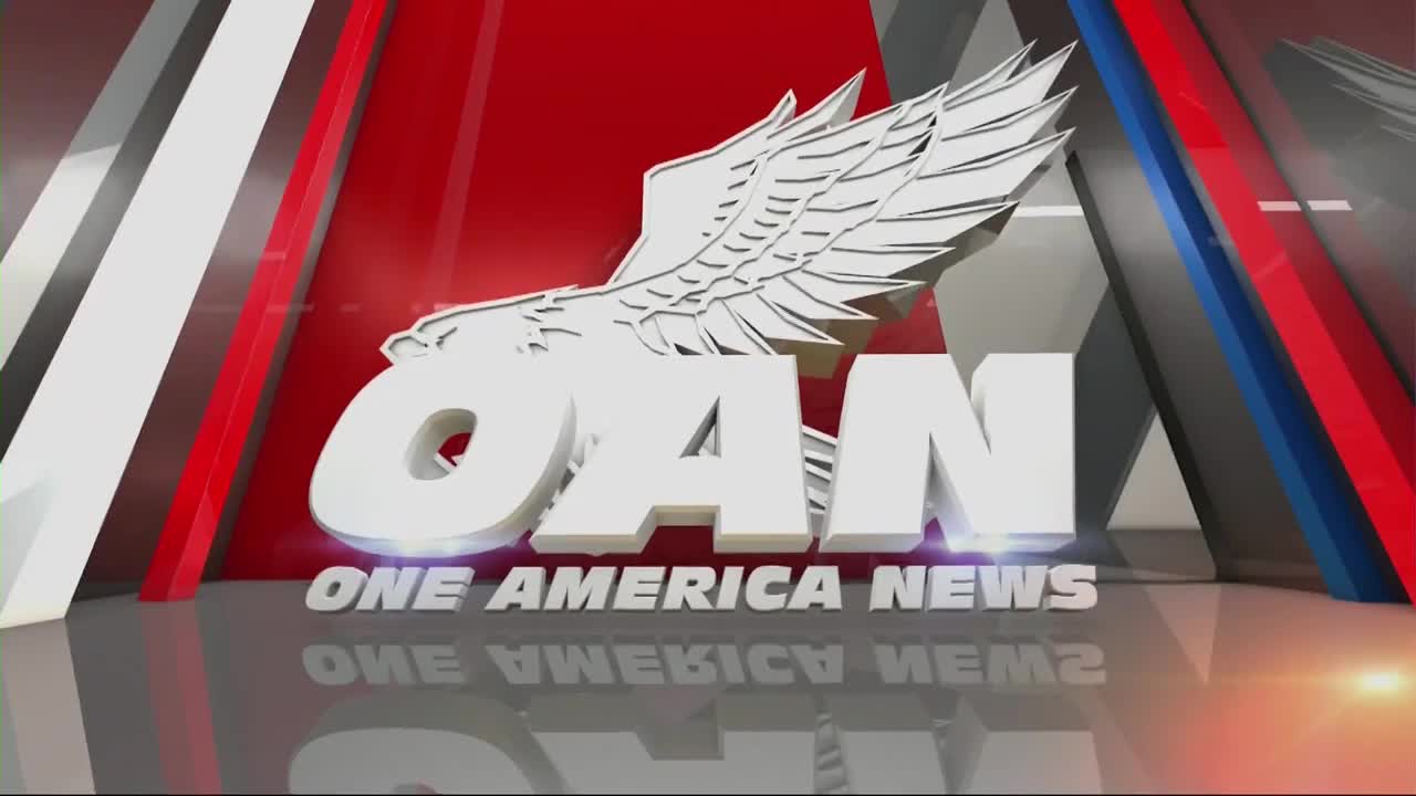 The large, metallic letters "OAN" with an eagle emblem hover over the words "ONE AMERICA NEWS." Red, white, and blue panels angle behind the logo, reflecting on the polished floor.
