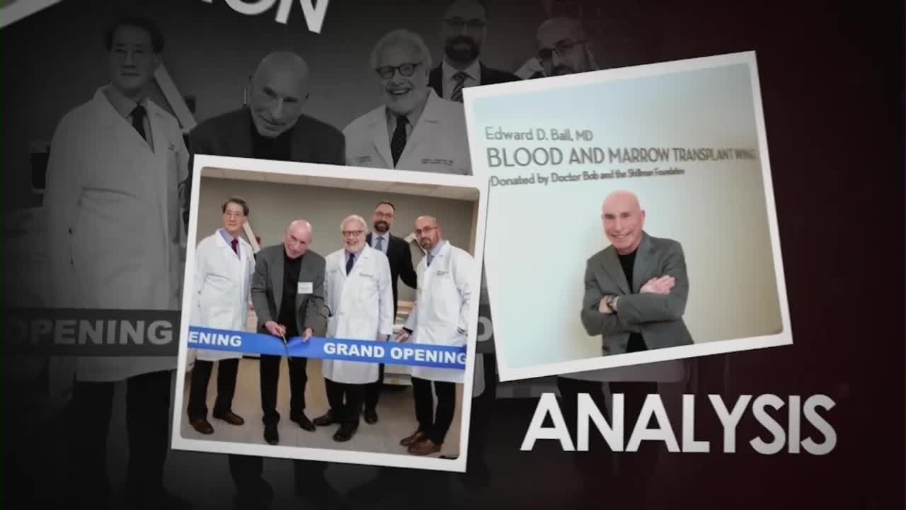 A man in a suit cuts a blue ribbon with scissors, flanked by doctors in white coats. A sign behind them announces the "Grand Opening" of the Edward D. Ball, MD Blood and Marrow Transplant Wing.