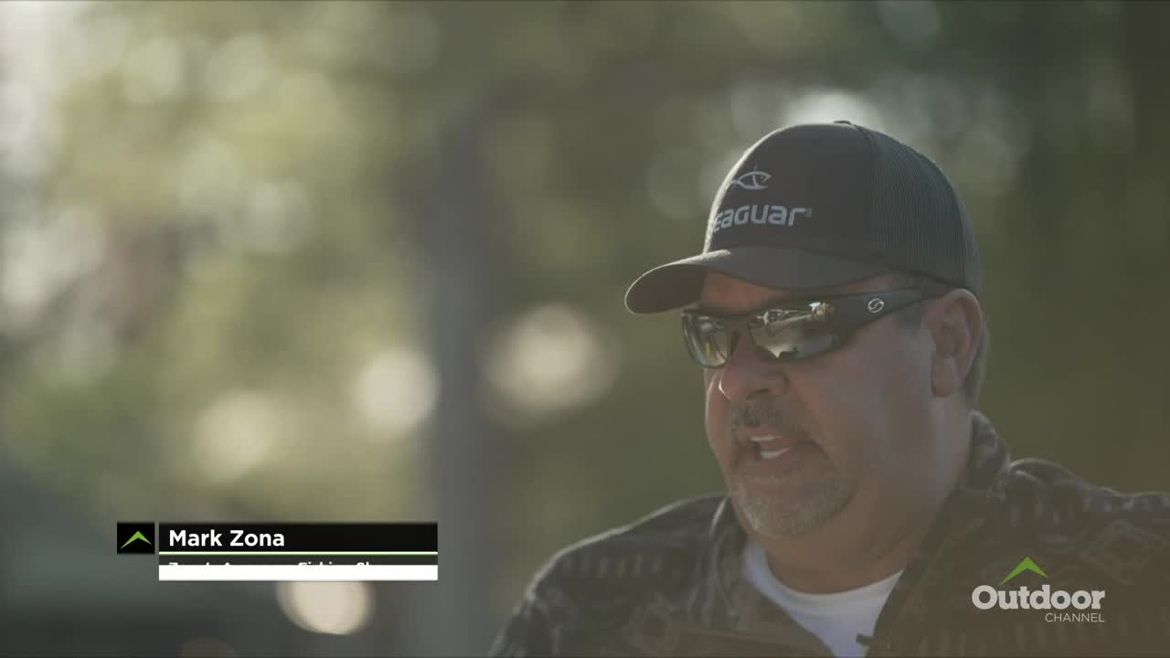 Mark Zona, wearing a cap and sunglasses, is talking to someone off-camera. The Outdoor Channel logo is visible in the corner.
