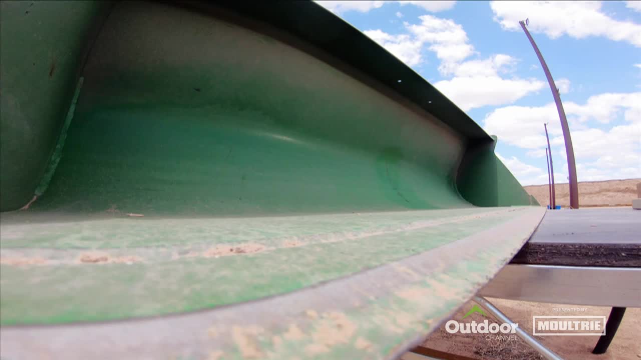 A curved, green metal structure stretches across the frame, its surface worn and dusty. Beyond it, against a bright sky, are some tall, thin metal poles.
