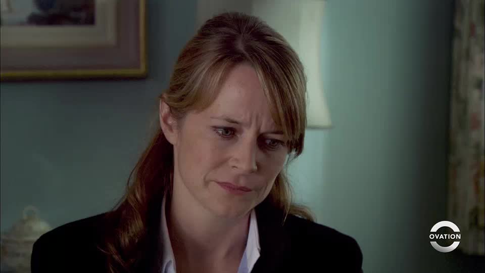 The woman's brow is furrowed, her gaze downcast. She's wearing a dark jacket, and the Ovation logo is visible in the corner.
