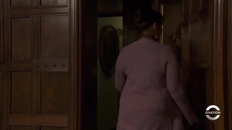 A woman in a pale pink cardigan walks through a dark wooden doorway. The Ovation logo is in the lower right corner.
