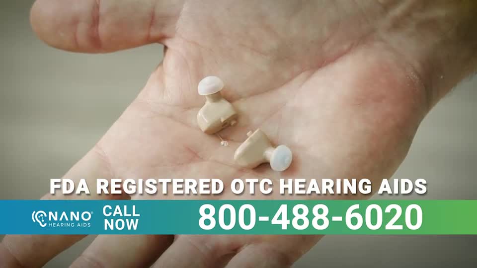 Two small beige hearing aids rest in an open palm. The devices appear to be in the palm of a hand, with a white tip on each.
