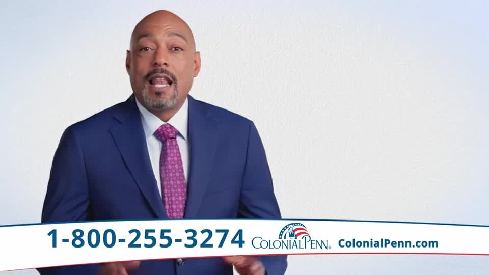 A man in a blue suit and patterned tie is speaking directly to the camera. Below him, a banner with a phone number and the Colonial Penn logo is displayed.
