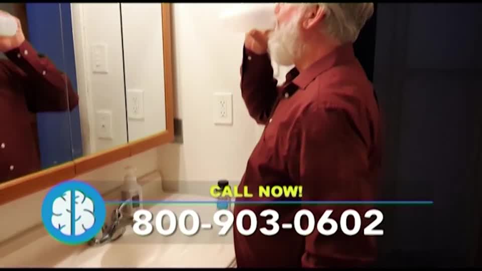 A man in a maroon shirt is mid-sip, holding a white container to his mouth. The bathroom mirror reflects the scene, and a phone number flashes at the bottom of the screen.
