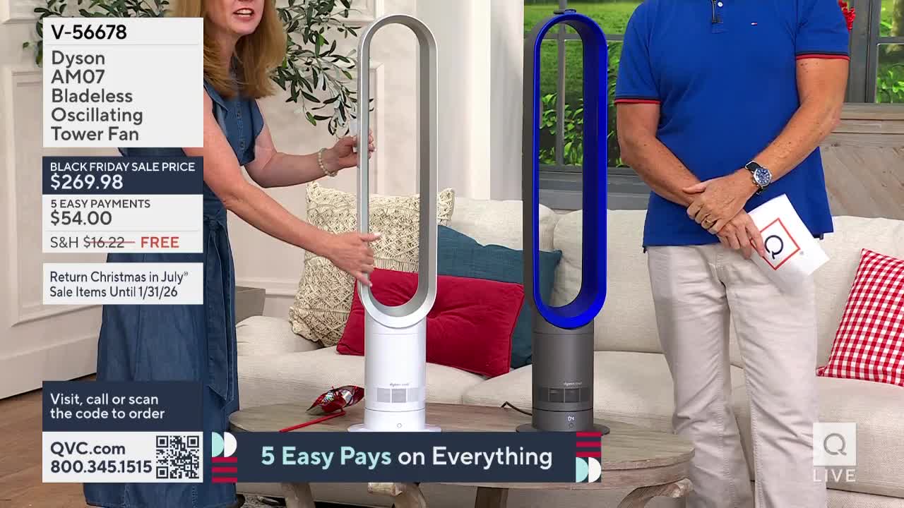 A woman in a denim dress holds up a white fan, while a man in a blue polo stands next to a blue one. The QVC studio is set up like a living room, with a couch and pillows in the background.
