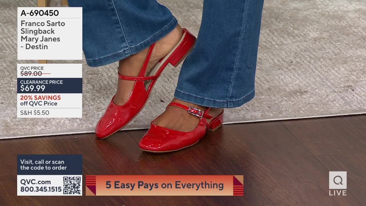 A pair of shiny red Mary Janes are shown, the straps and buckles catching the light. The shoes are on display during a QVC presentation, with a price tag visible in the corner.
