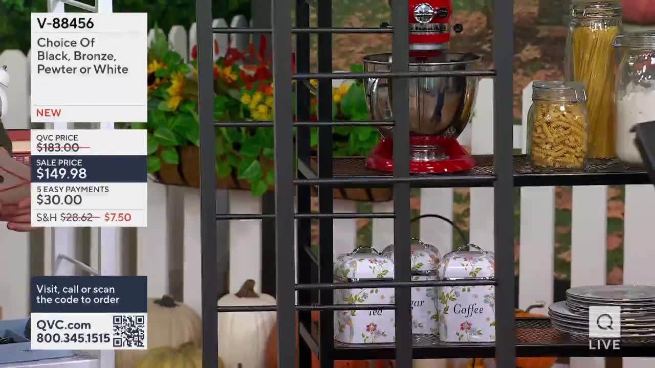 A red stand mixer sits on a shelf, next to jars of pasta and flour. The QVC price for the mixer is listed on a screen to the left.
