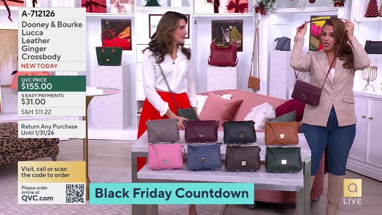 Two women on a QVC set are showcasing different colors of a Dooney & Bourke crossbody bag. One presenter holds up a burgundy bag, adjusting the strap as she demonstrates its length.

