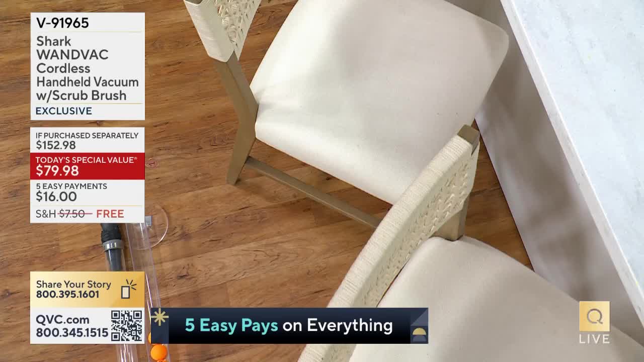 A vacuum cleaner attachment rests on the floor next to two chairs. The QVC logo and product information are displayed on the screen.
